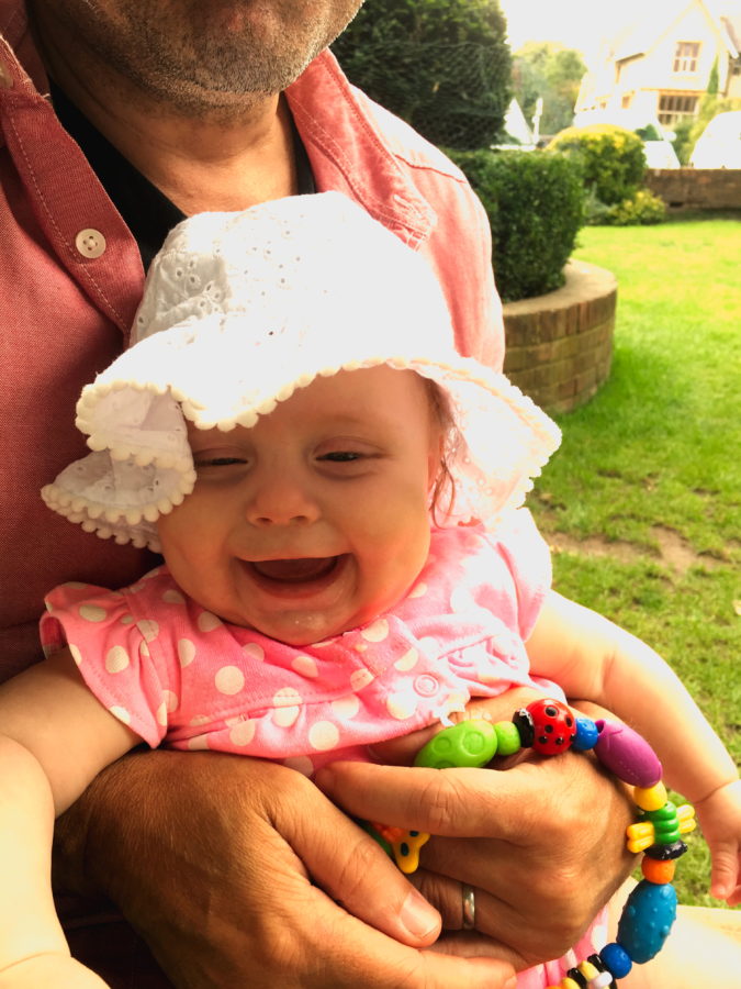 Baby sitting on someone's lap, with a sunhat on, with grass in the background, laughing