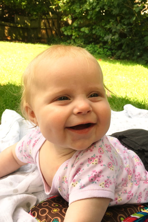 Baby lying on her tummy on a rug on the grass, smiling