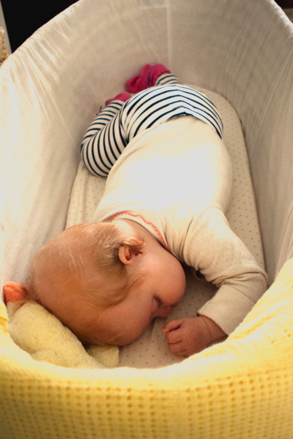 baby asleep on her tummy in a moses basket in stripy leggings and a white top