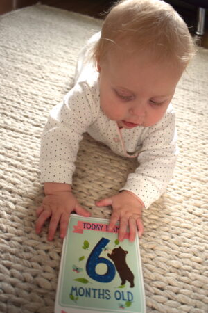 baby lying on tummy holding card saying today I am six months old