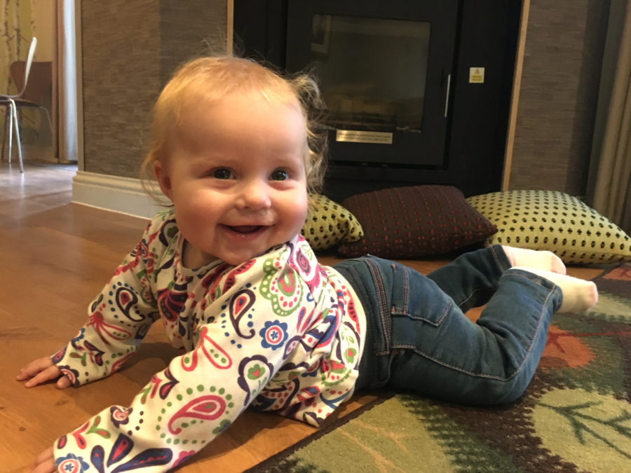 baby lying on tummy, holding chest and head up, smiling, in front of a fireplace