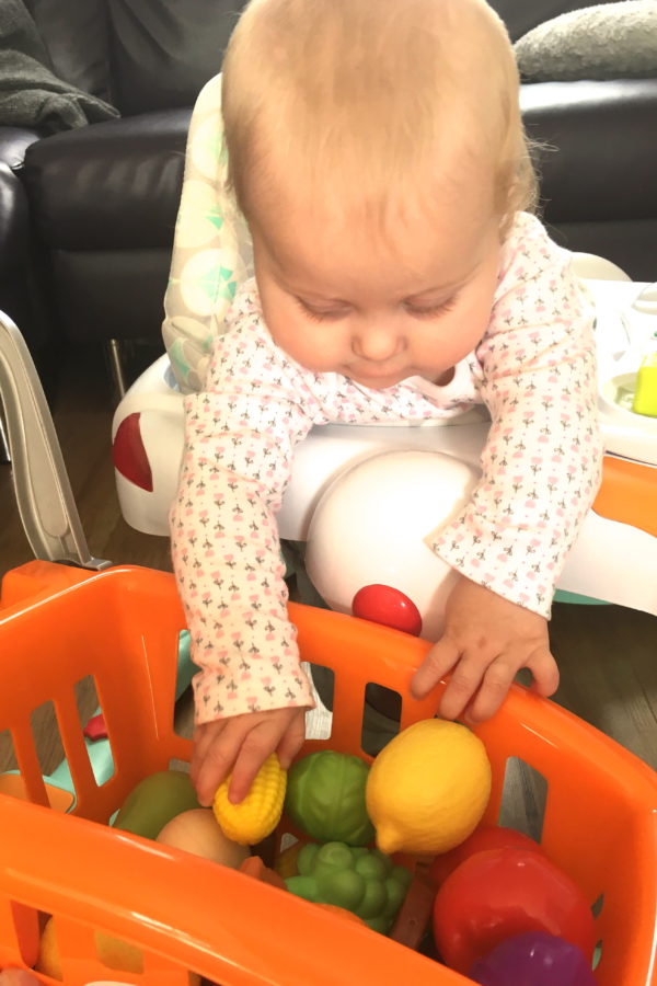 baby leaning out of walker, playing with trolley of plastic fruit and veg