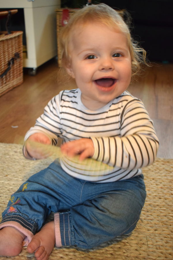 nine month old baby girl in stripy top and jeans, holding a card and laughing