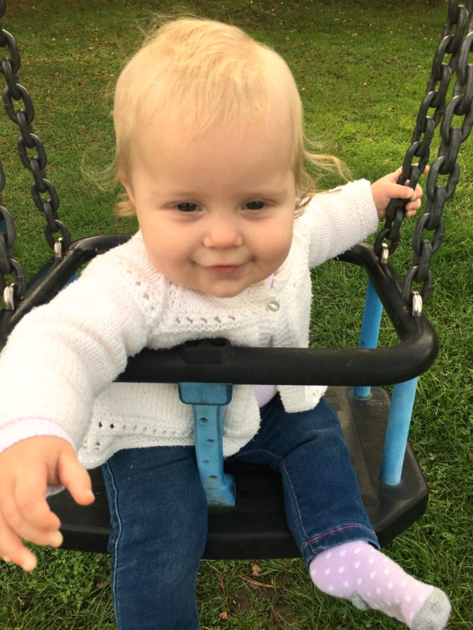 baby girl sitting on park swing, smiling