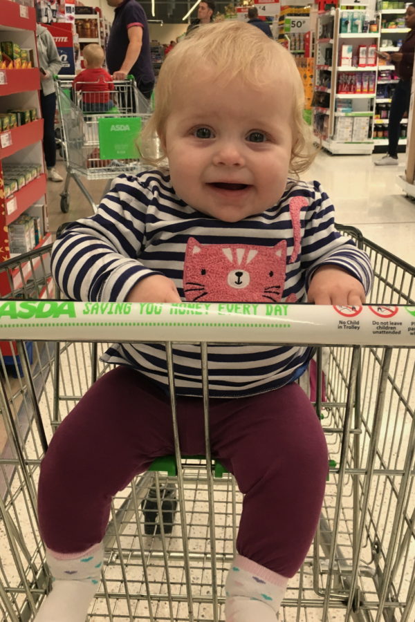 baby in a stripey top, sitting in supermarket trolley, smiling
