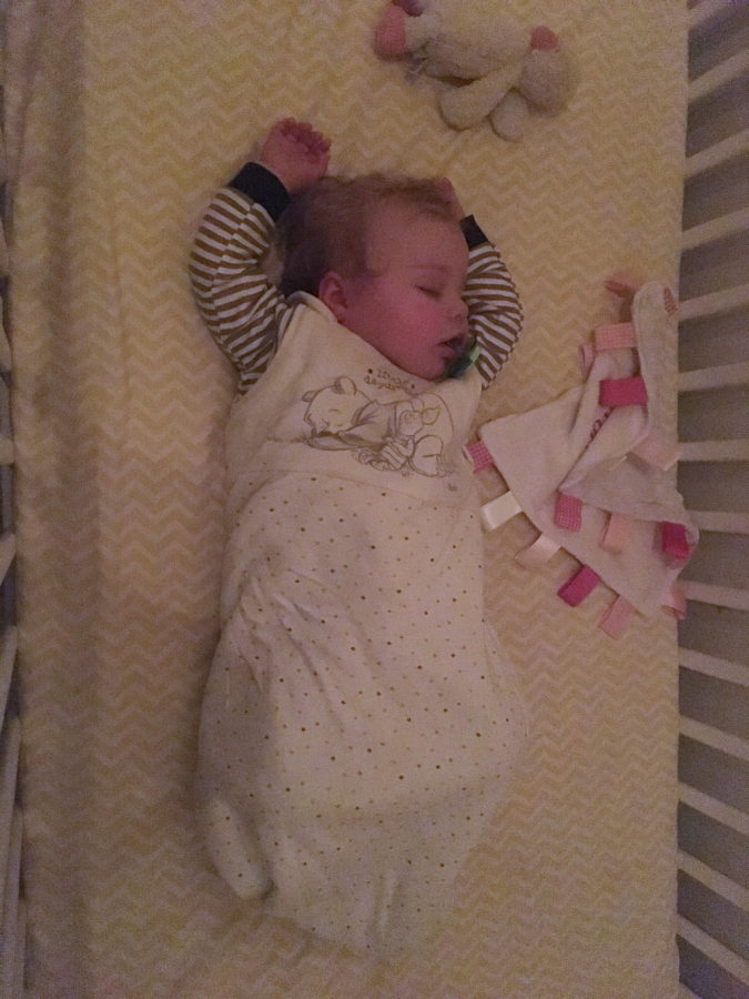 baby asleep in cot, lying on back with hands above head