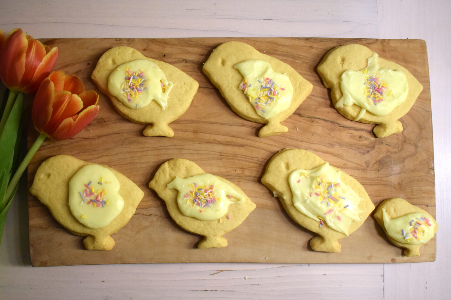 dairy and soya free Easter cookies in shape of chicks on wooden board with tulips