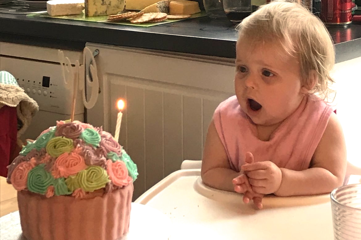 one year old looking at birthday cake in surprise
