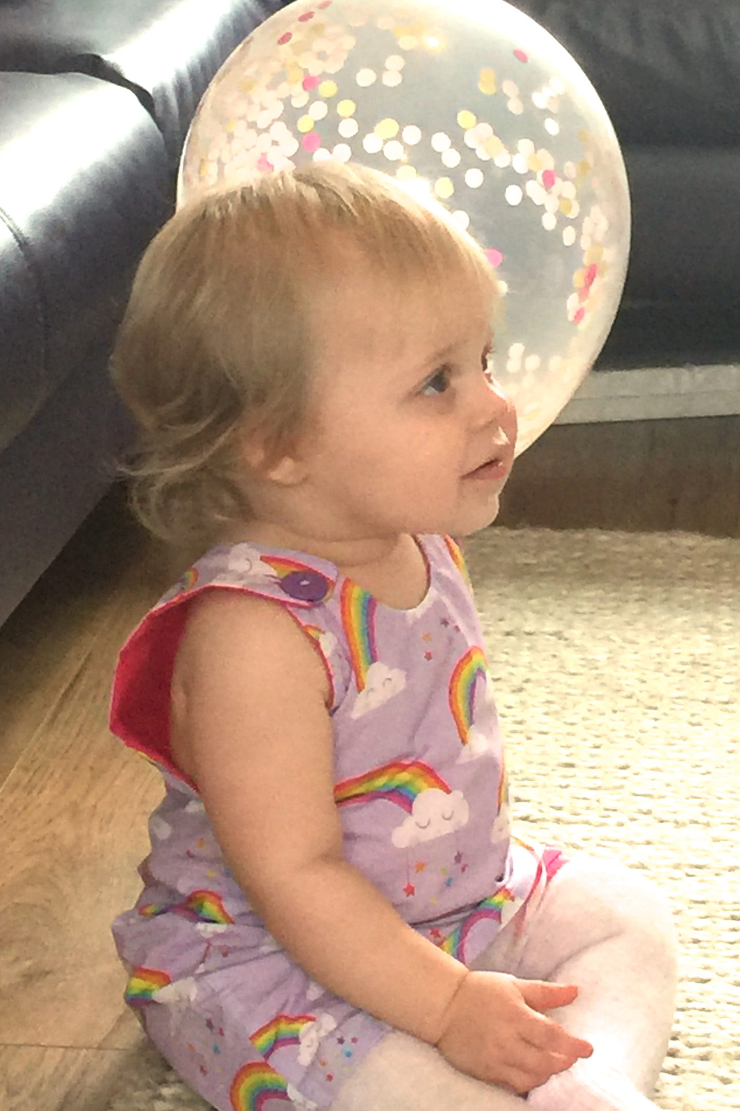 one year old in party dress sitting on the floor, holding a balloon