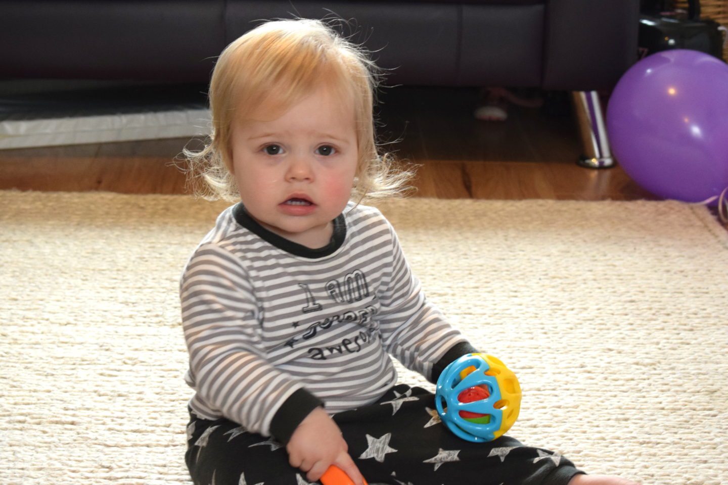 one year old girl in pyjamas, sitting on a rug, holding a ball