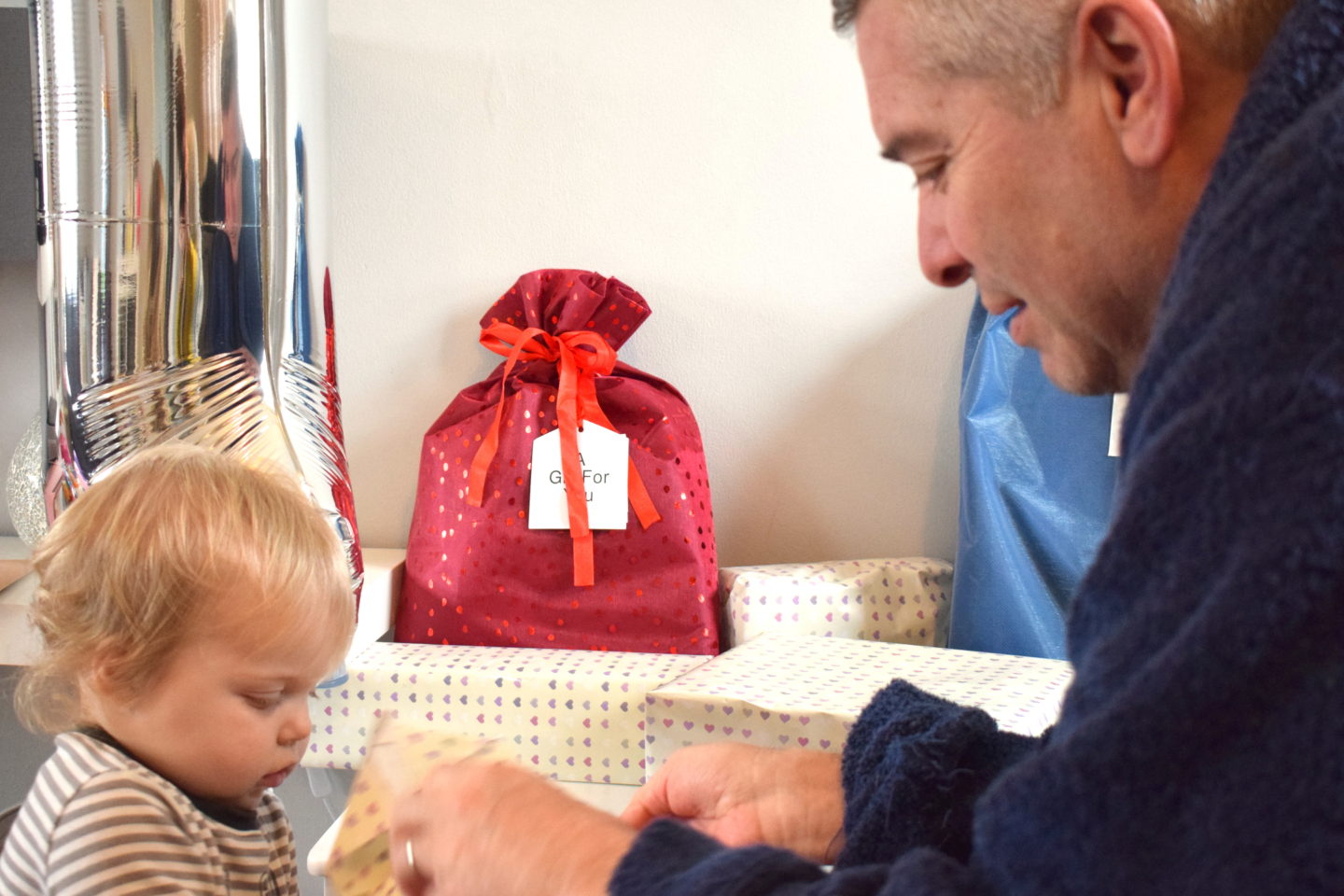 one year old girl standing with dad, opening birthday present