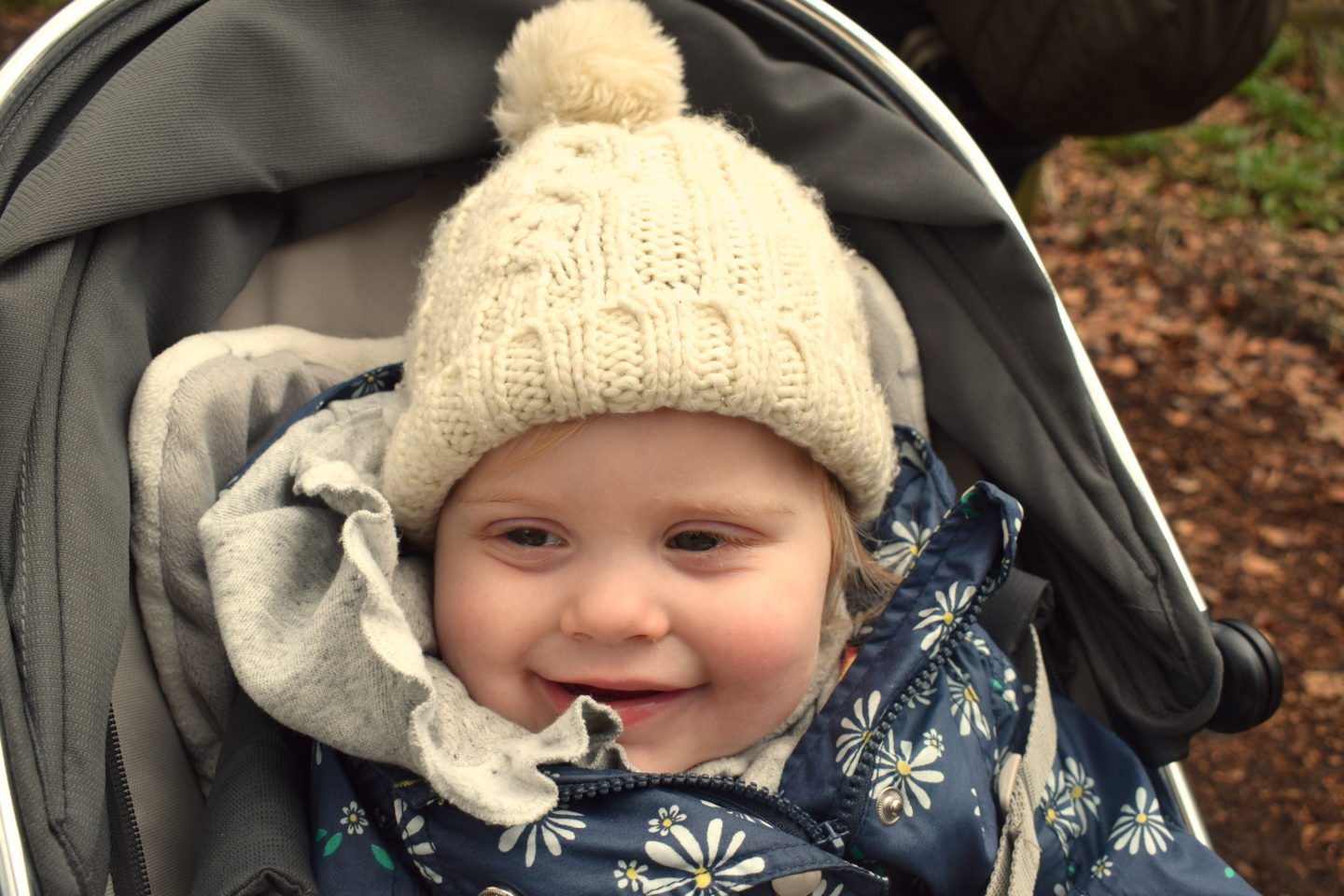 14 months old girl with bobble hat, sitting in pram, smiling