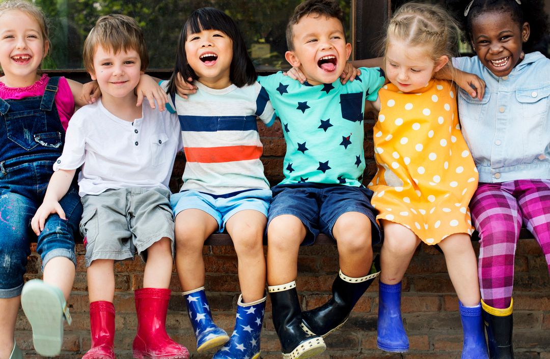 six young children socialise while sitting together on a bench, laughing