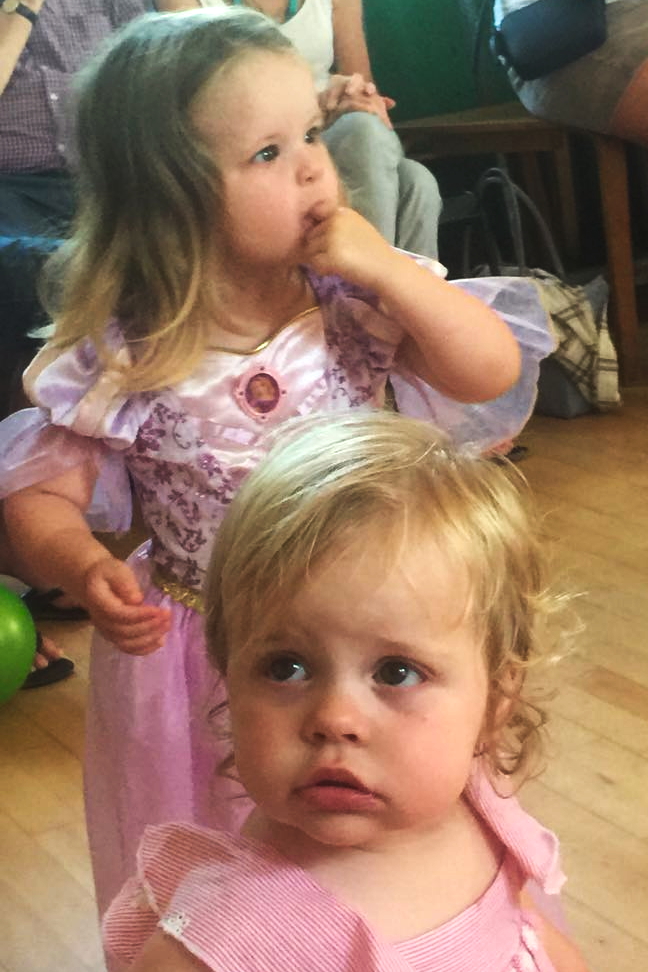 Two and one year old sisters at a party, dressed in pink