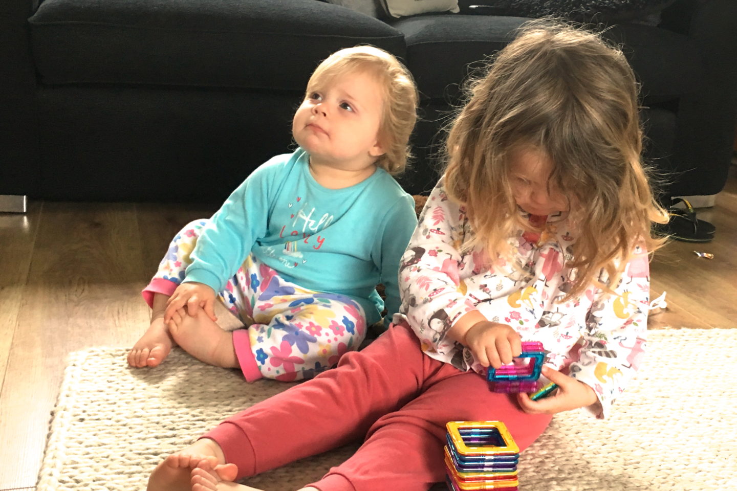 two and one year old sisters sitting together on a rug