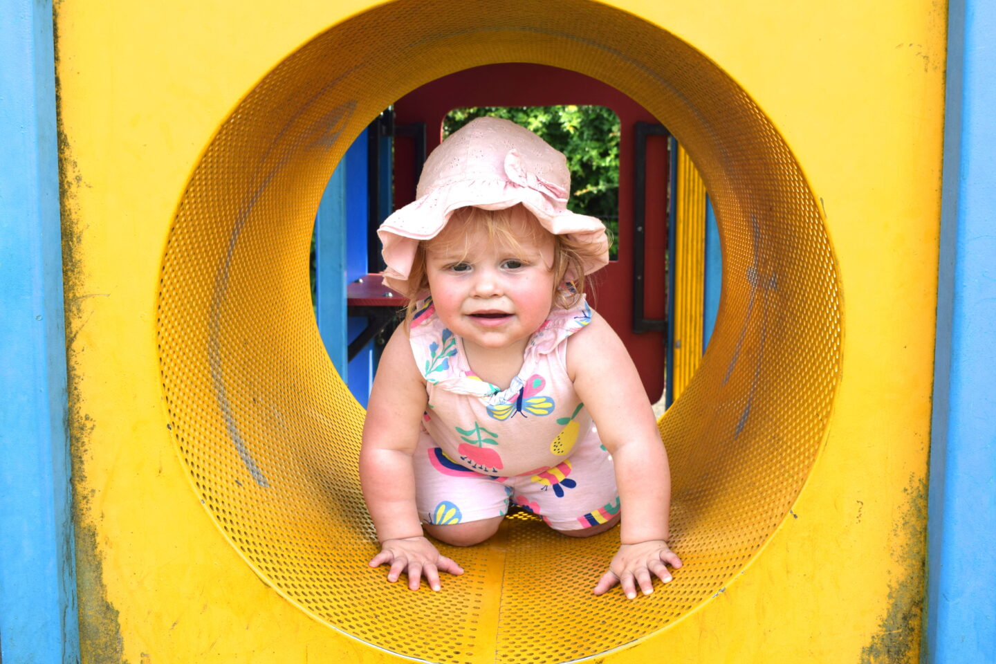 Toddler girl climbing through tunnel at the park, having some family downtime