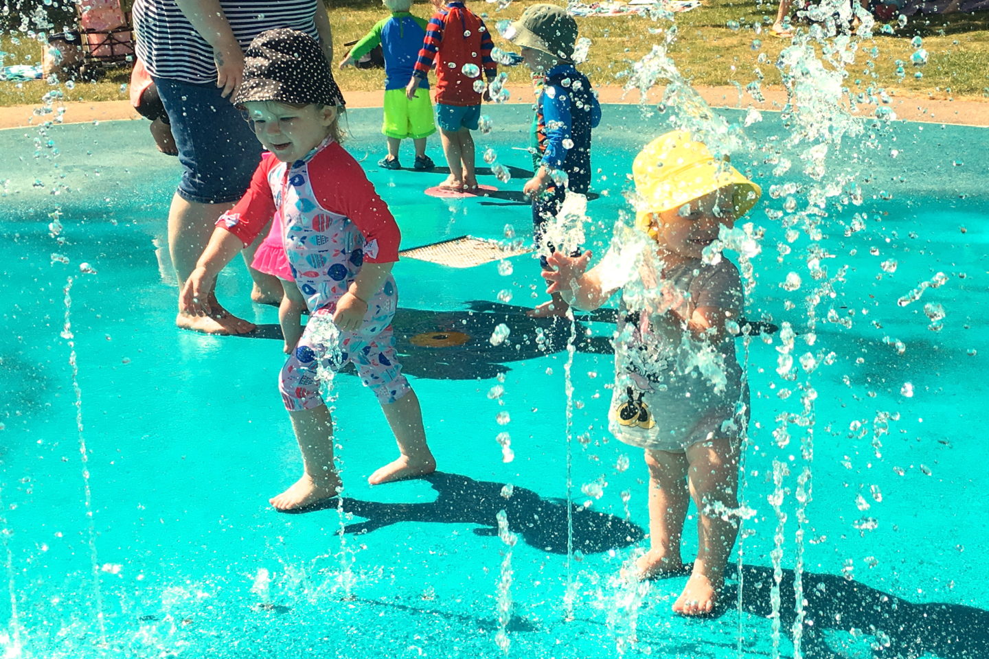 two toddler sisters playing in the jets at a splash park
