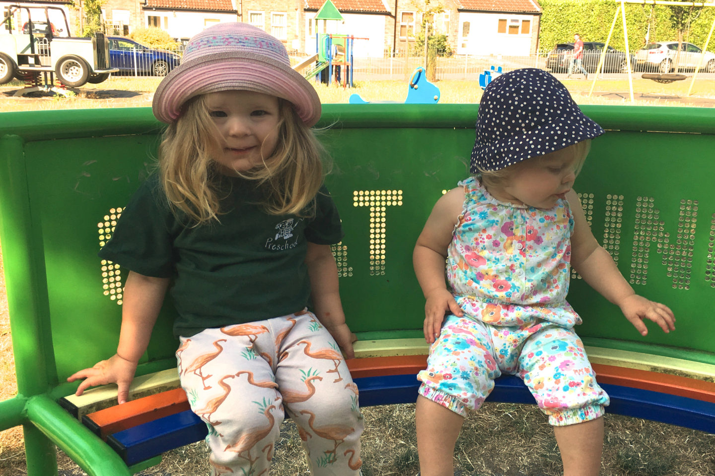 two year old and one year old sisters sitting together on a roundabout
