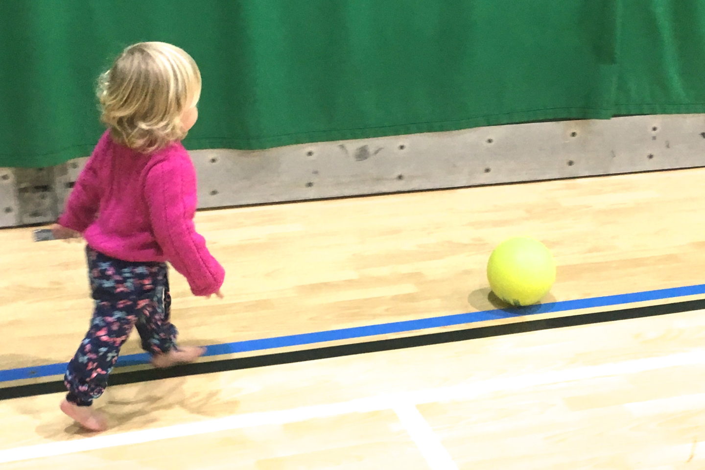 18 month old girl chasing ball in sports hall