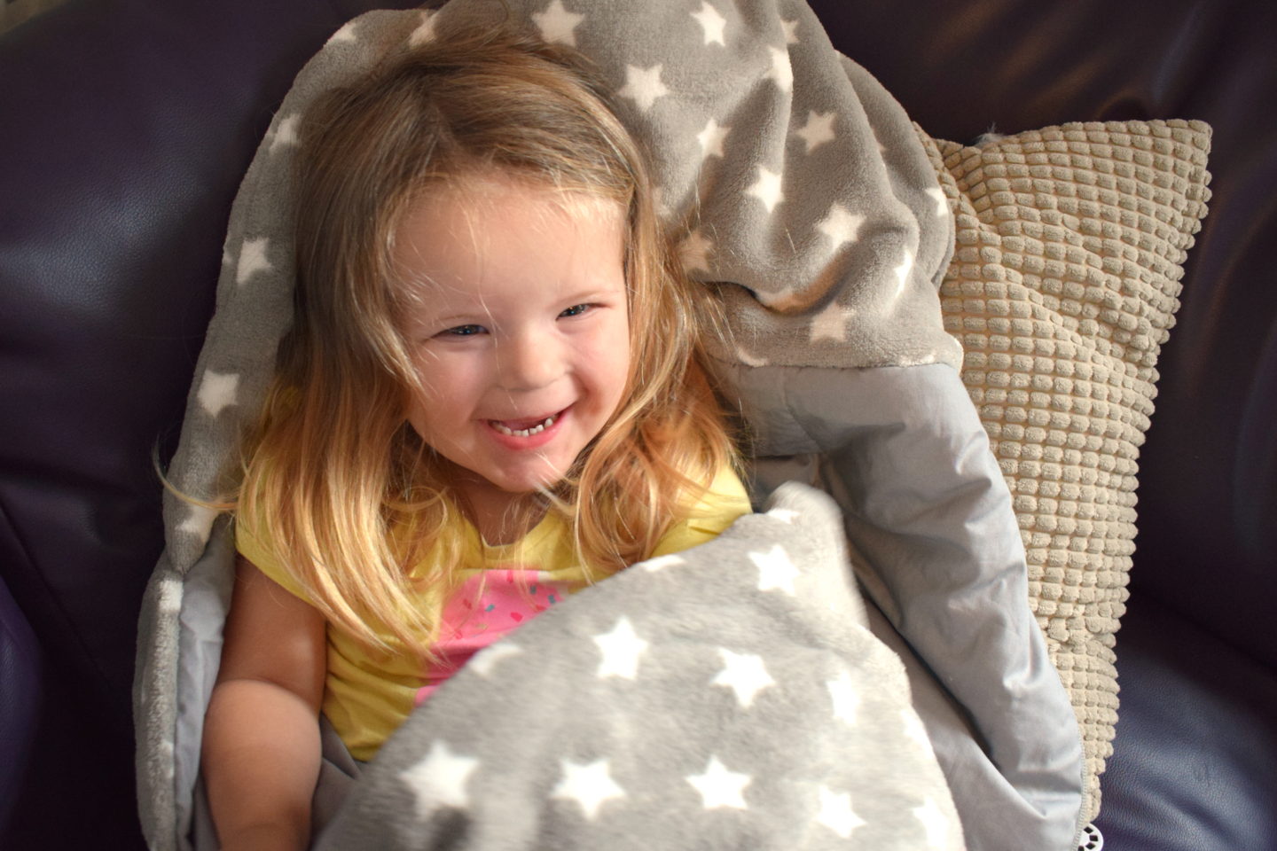 three year old girl in Snuggle Sac on sofa, laughing