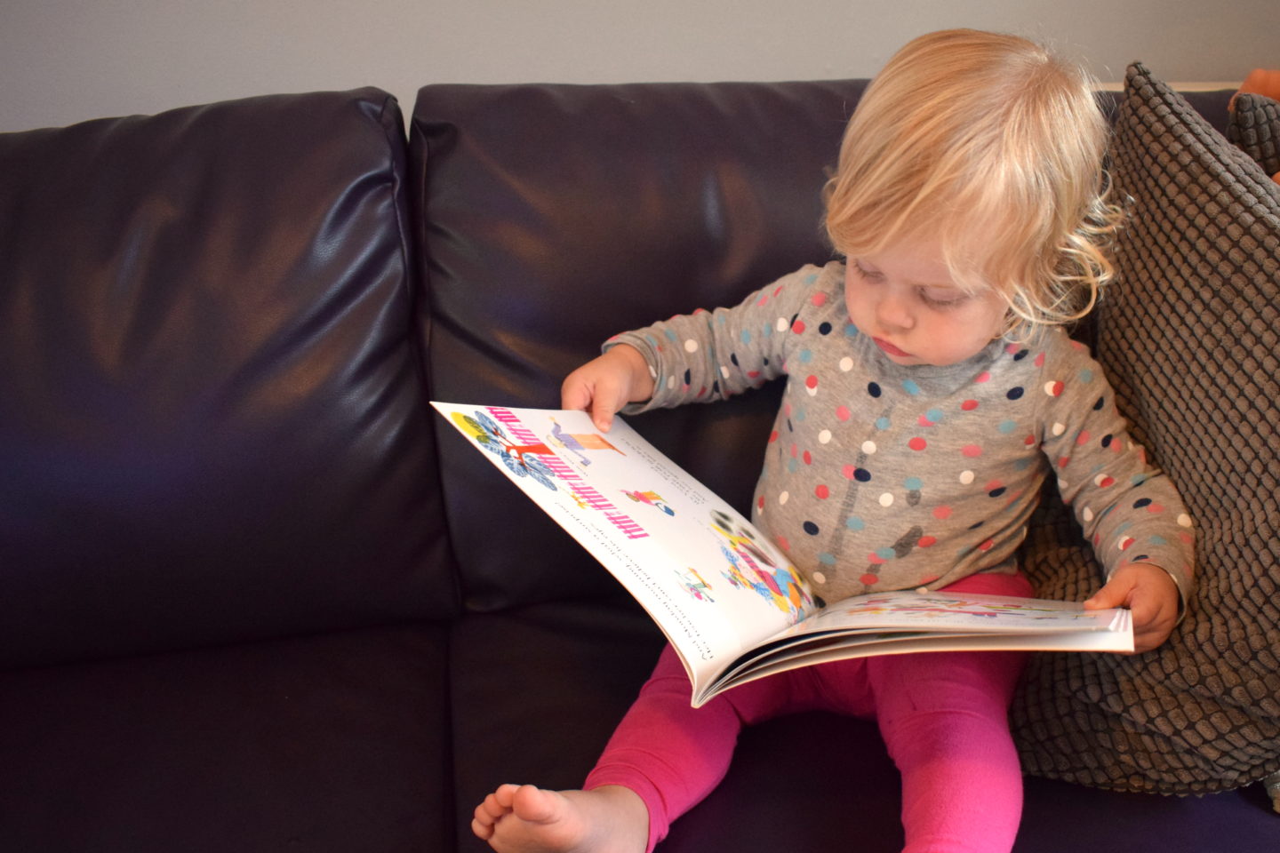 18 month old girl reading a book on the sofa - time to read