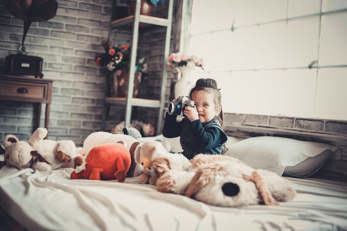 toddler girl, sitting on bed with cuddly toys, taking a photograph - when kids share a room