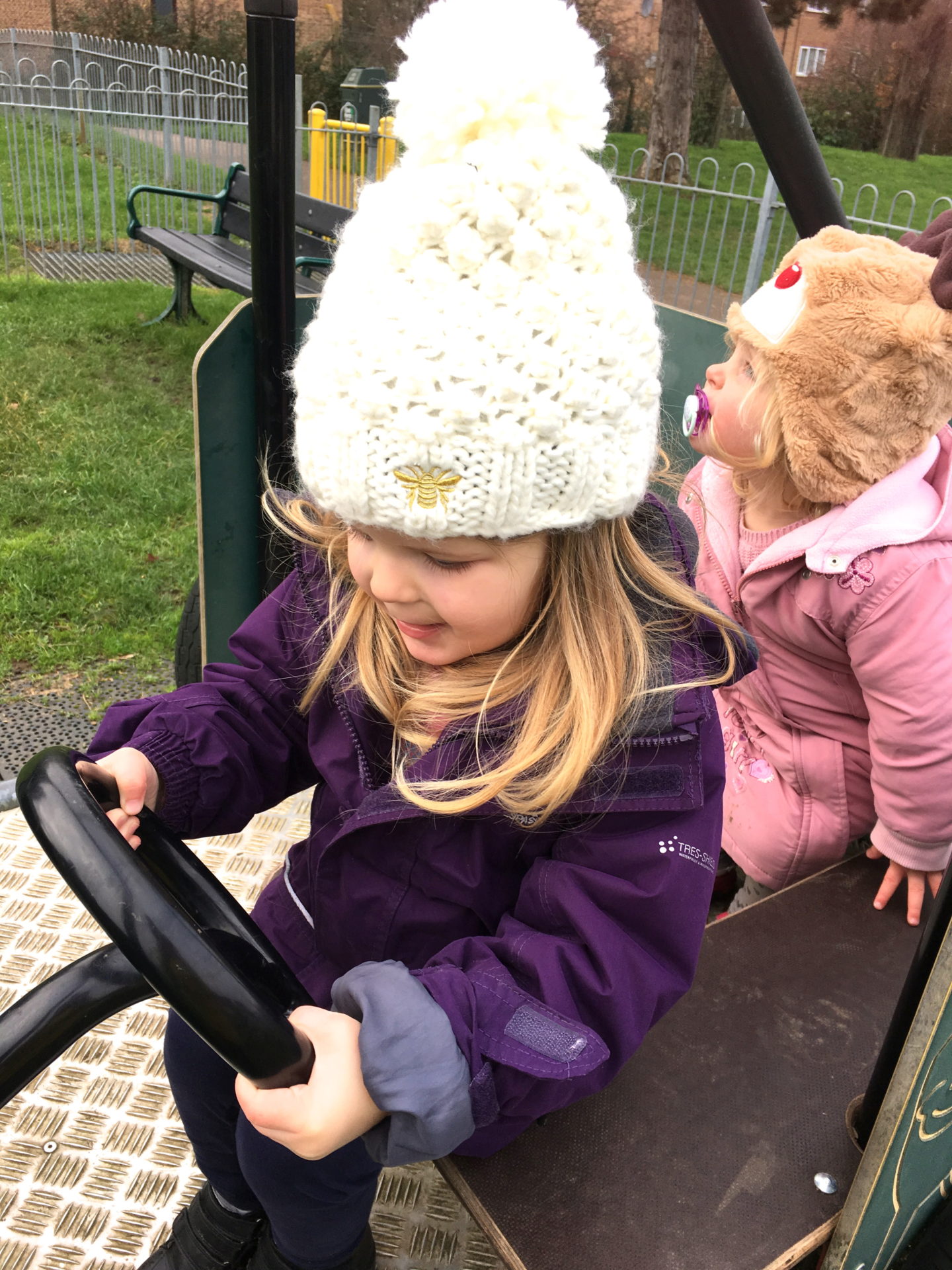 two sisters sitting on a climbing frame car, one pretending to drive
