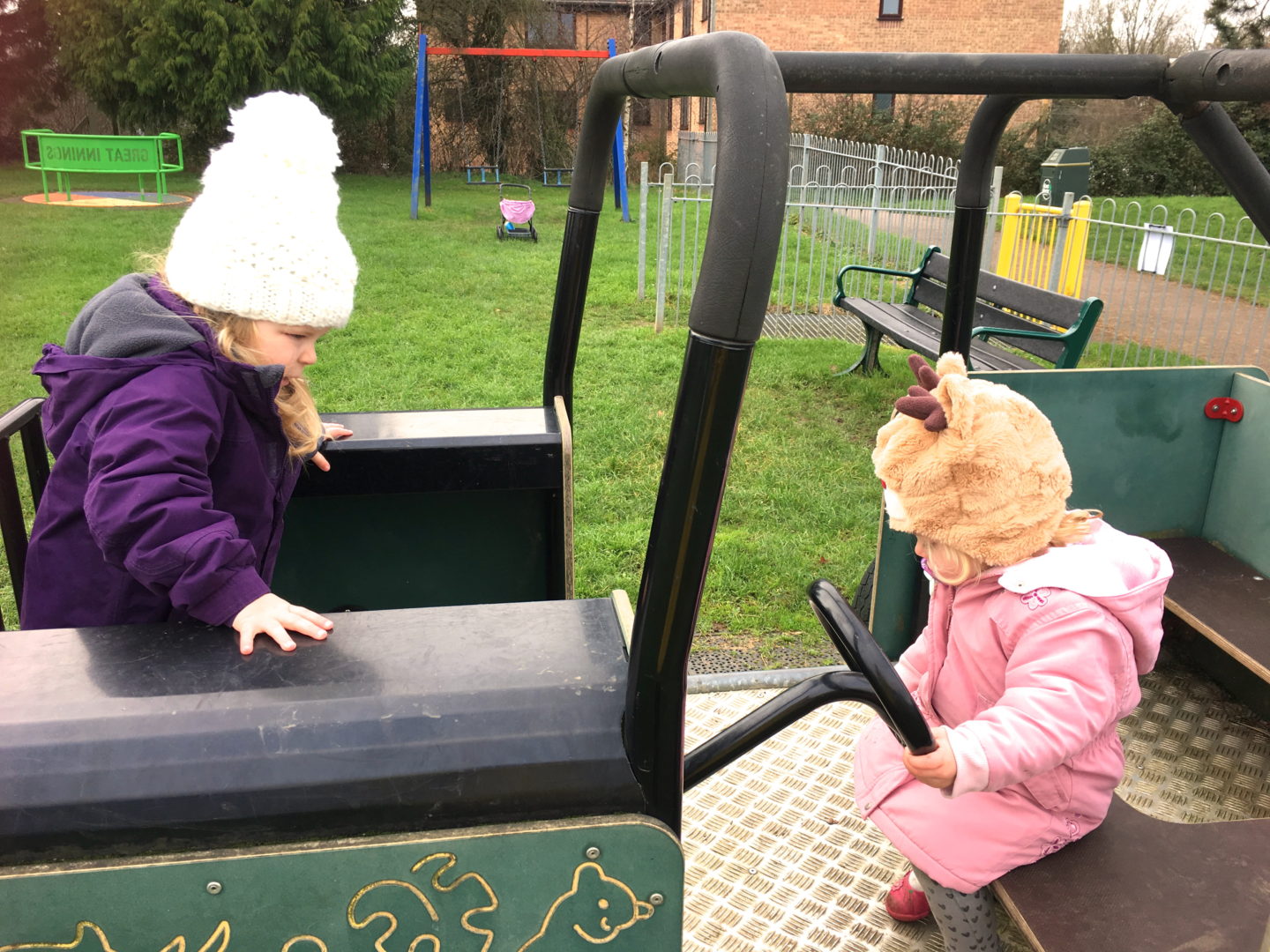 Two toddler sisters playing on a climbing frame car in a playground