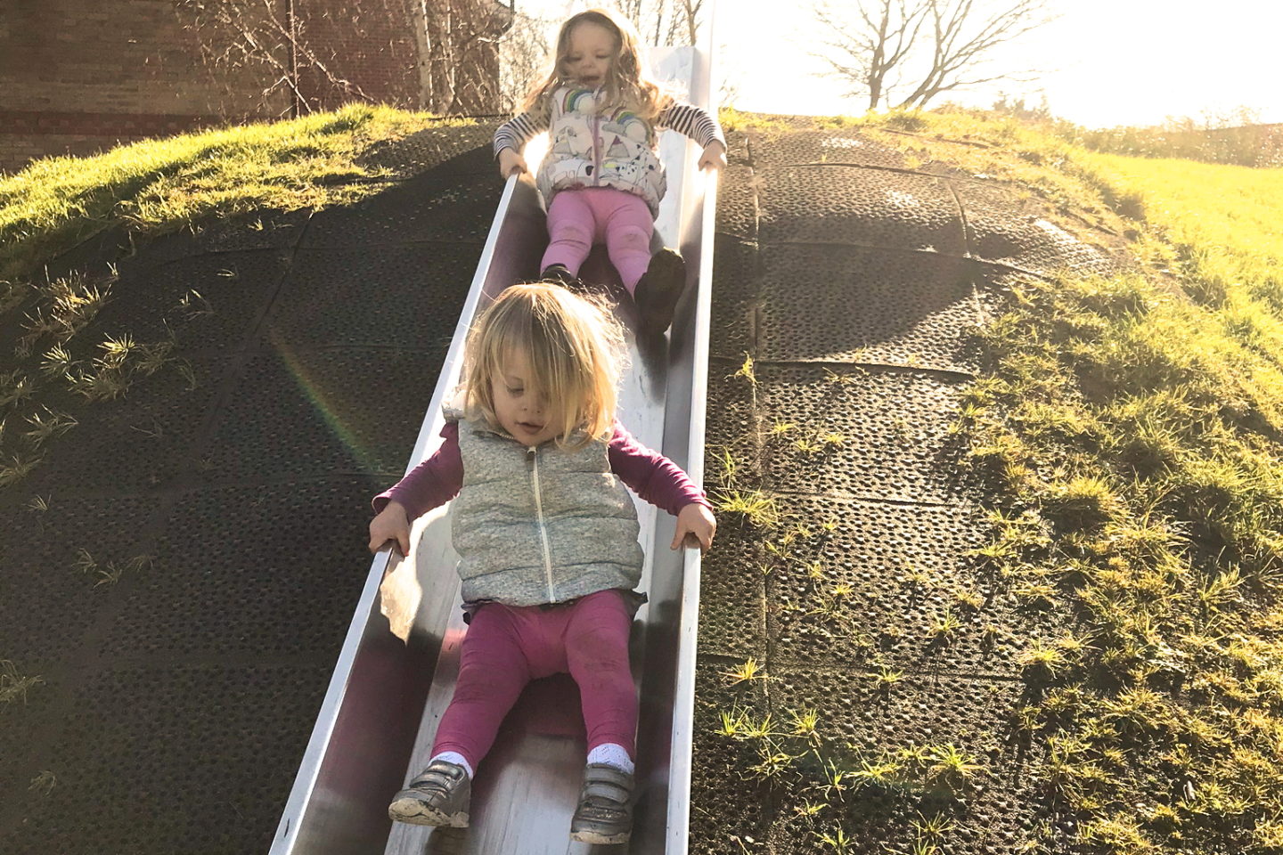 Two sisters going down a slide behind one another