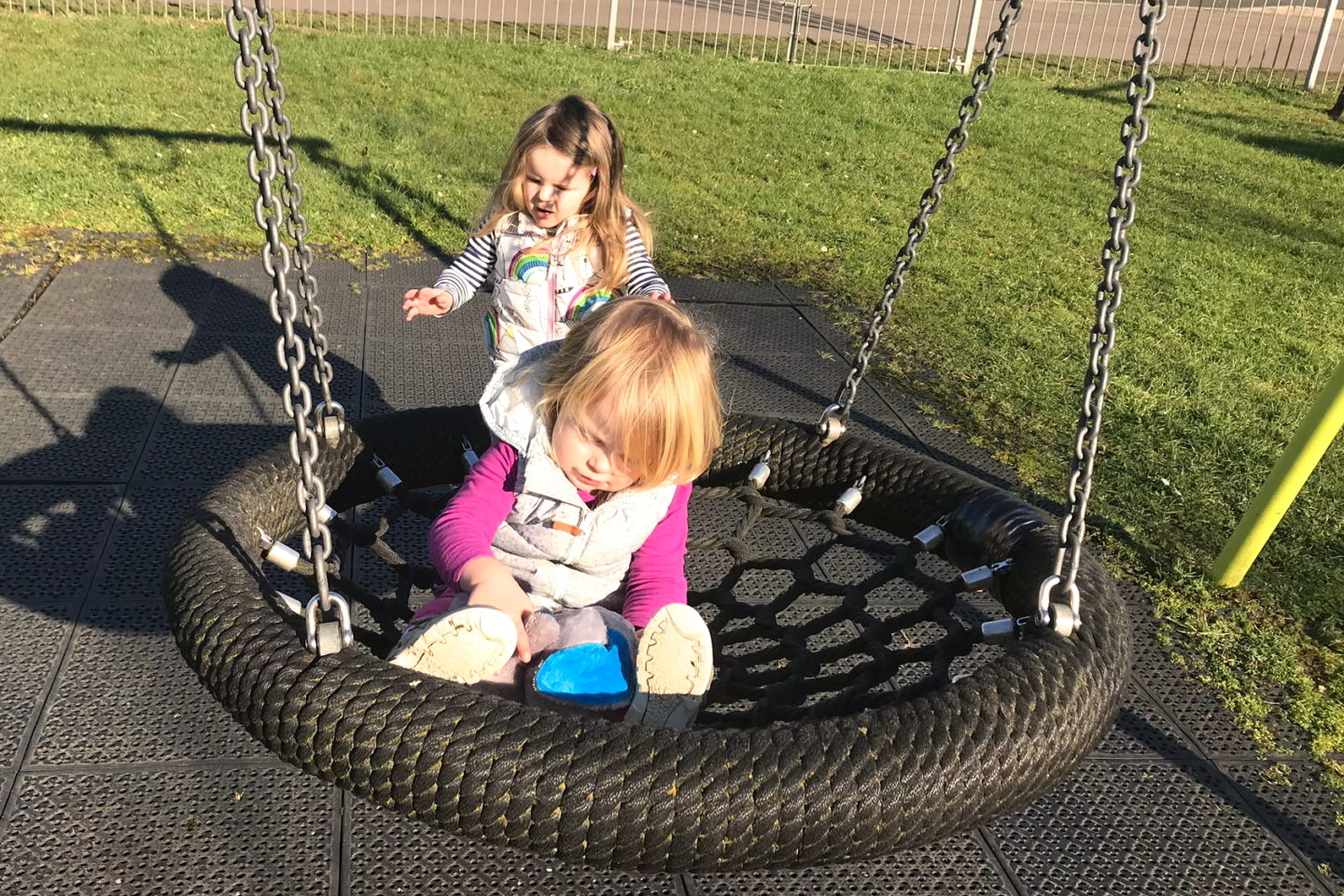 toddler sitting on a net swing with big sister pushing her
