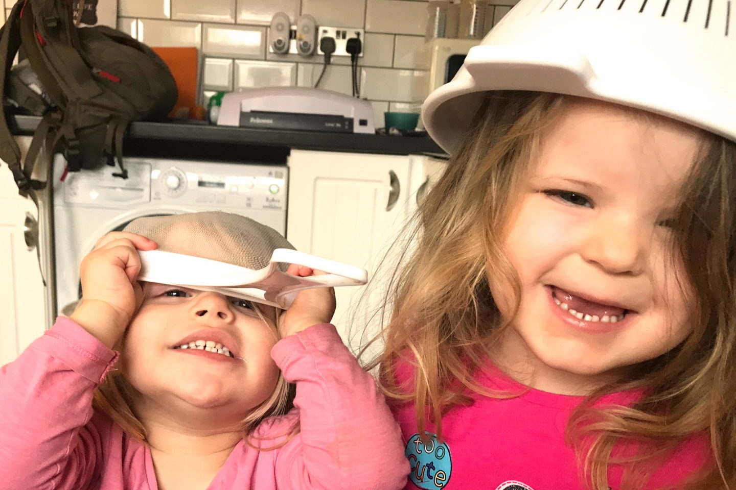 two young sisters laughing with sieves on their heads