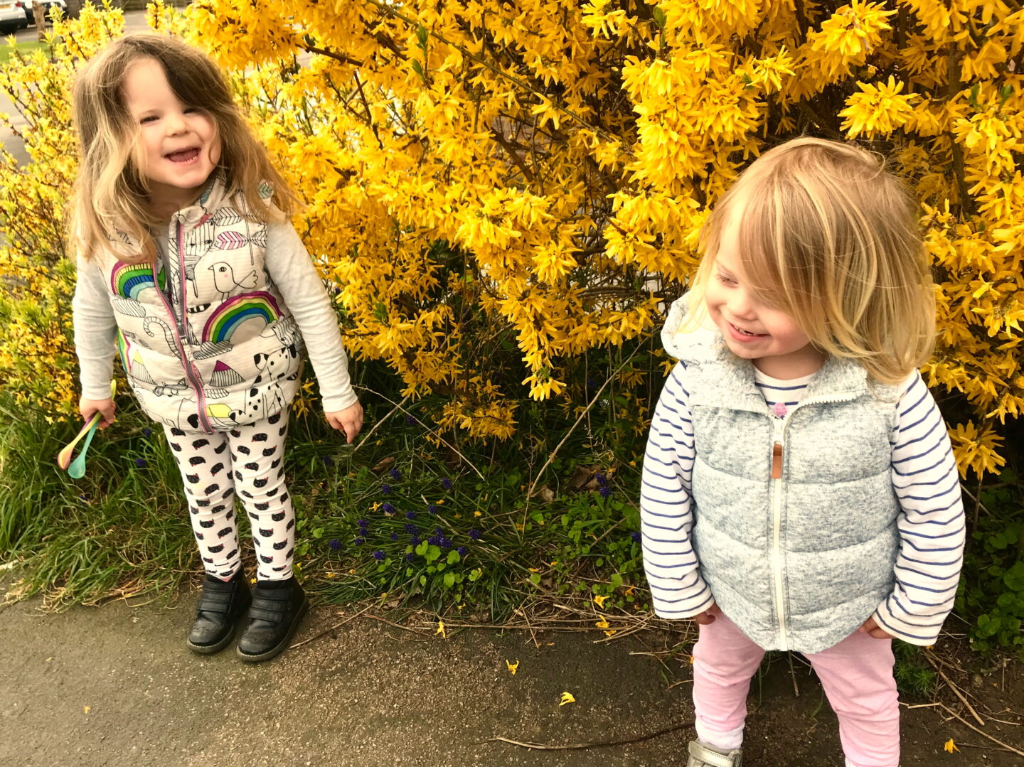 Two sisters standing in front of a yellow flowering bush, smiling