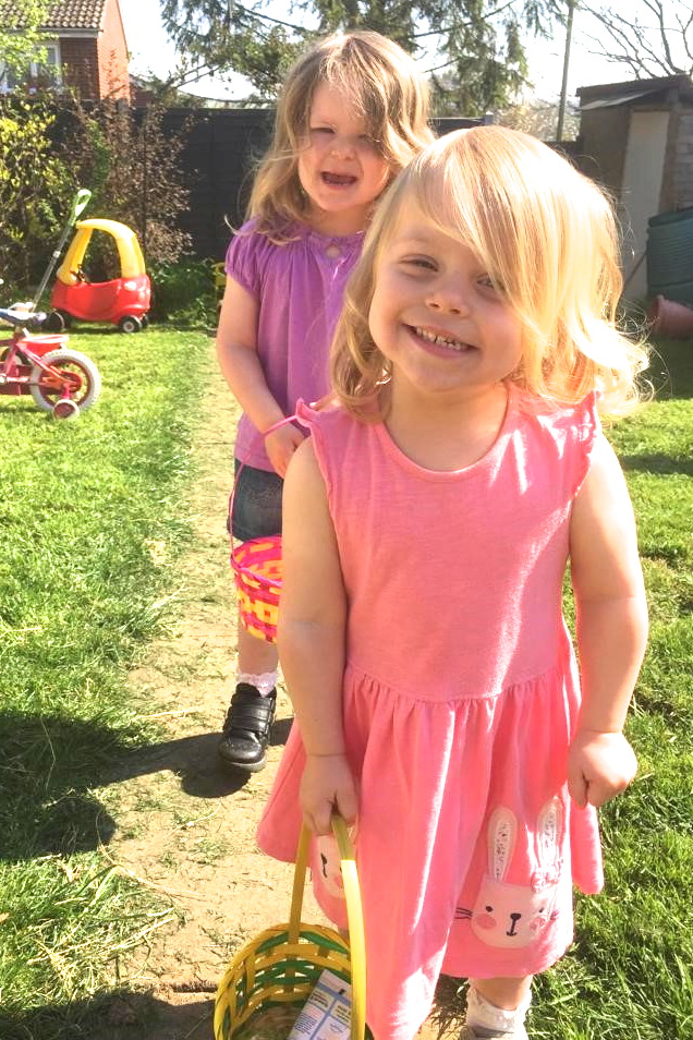 two young sisters holding baskets doing an easter egg hunt in the garden
