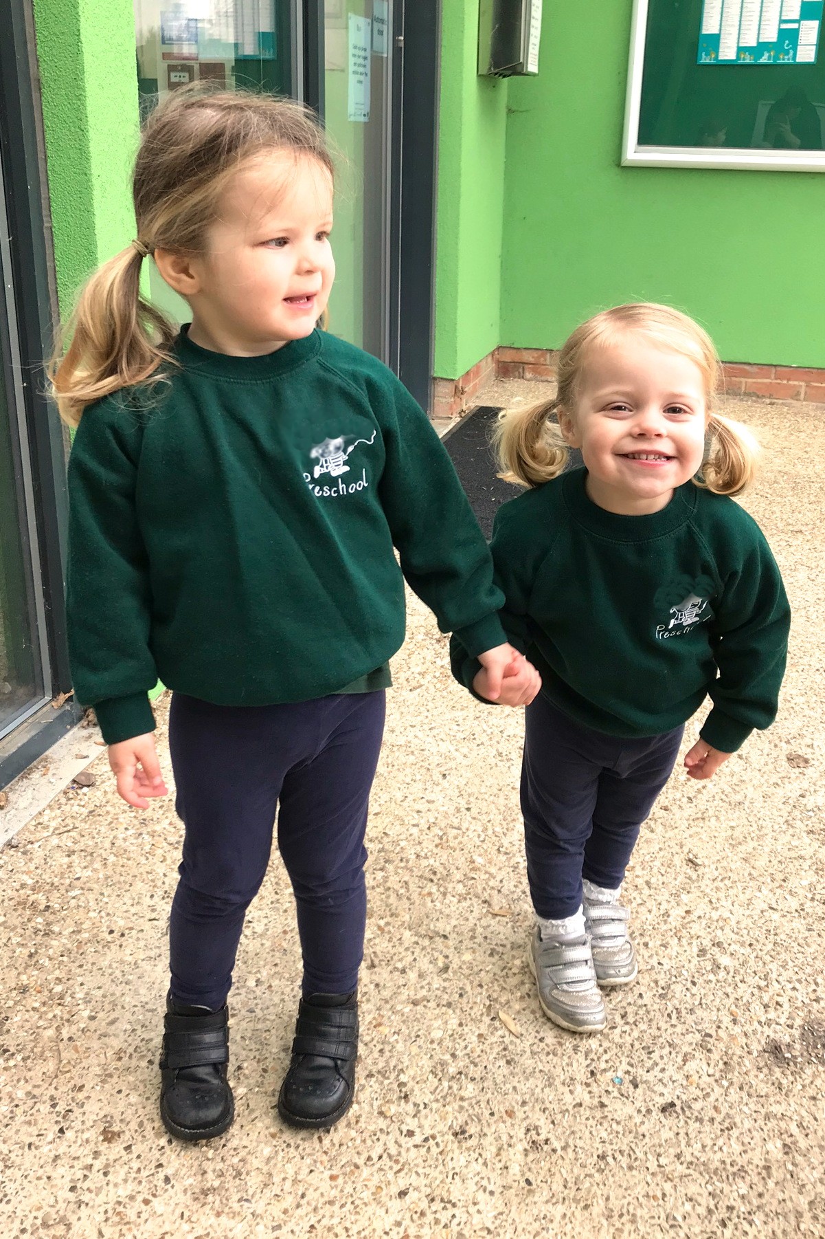 two sisters holding hands in preschool uniform, smiling
