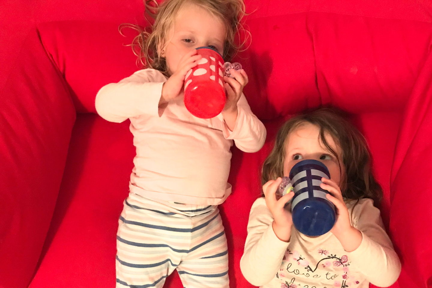 Two sisters in pyjamas, drinking milk, lying on a sofa