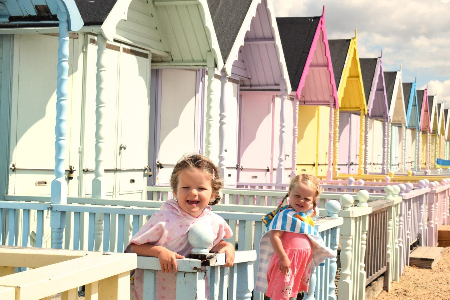 two little girls on the decking of a beach hut, leaning on the balustrade