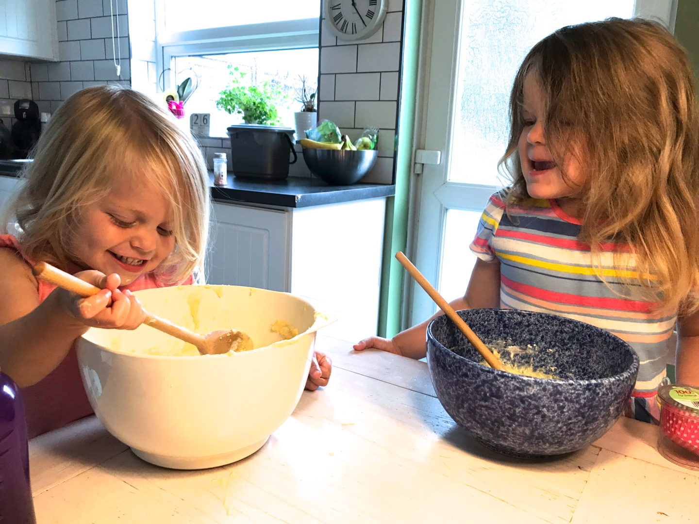 two little sisters, sitting at a table with a mixing bowl and wooden spoon each