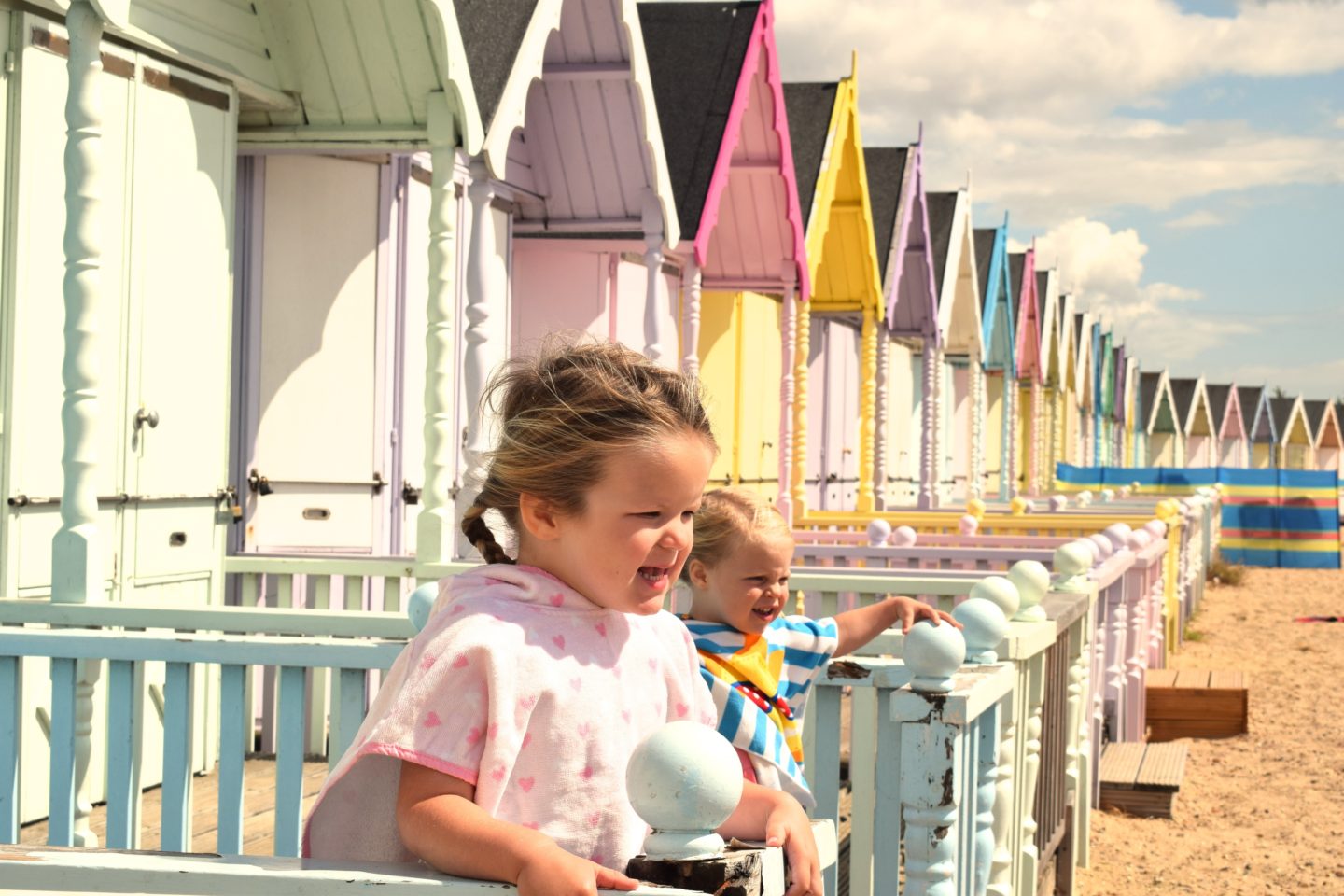 two little sisters on the decking of a beach hut, leaning on the balustrade