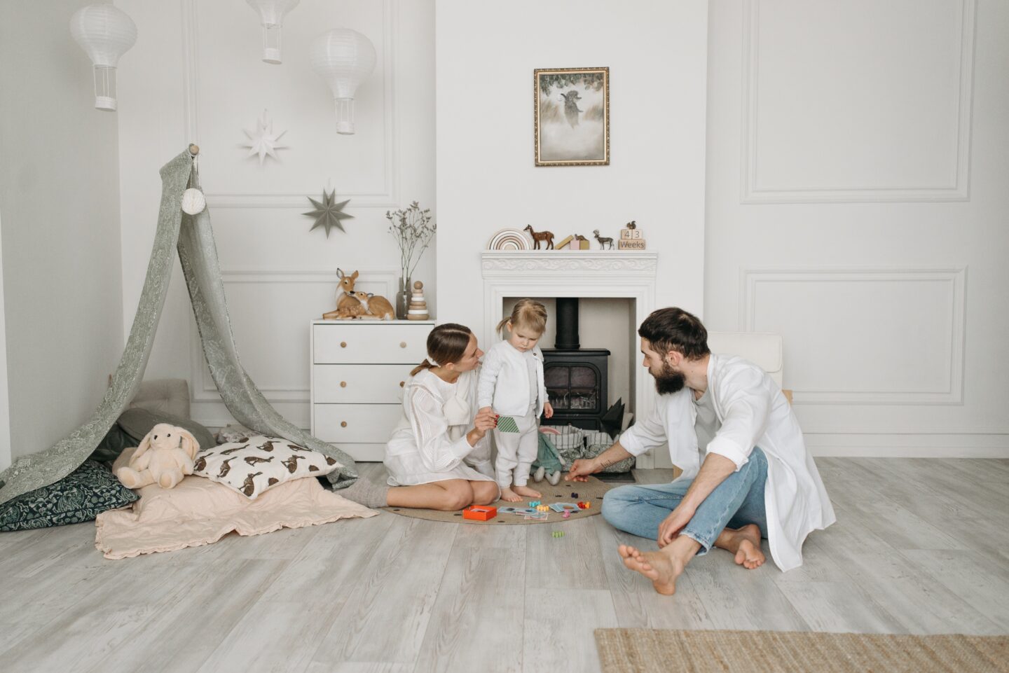Family of three playing on the floor of a child's bedroom with teepee in the background